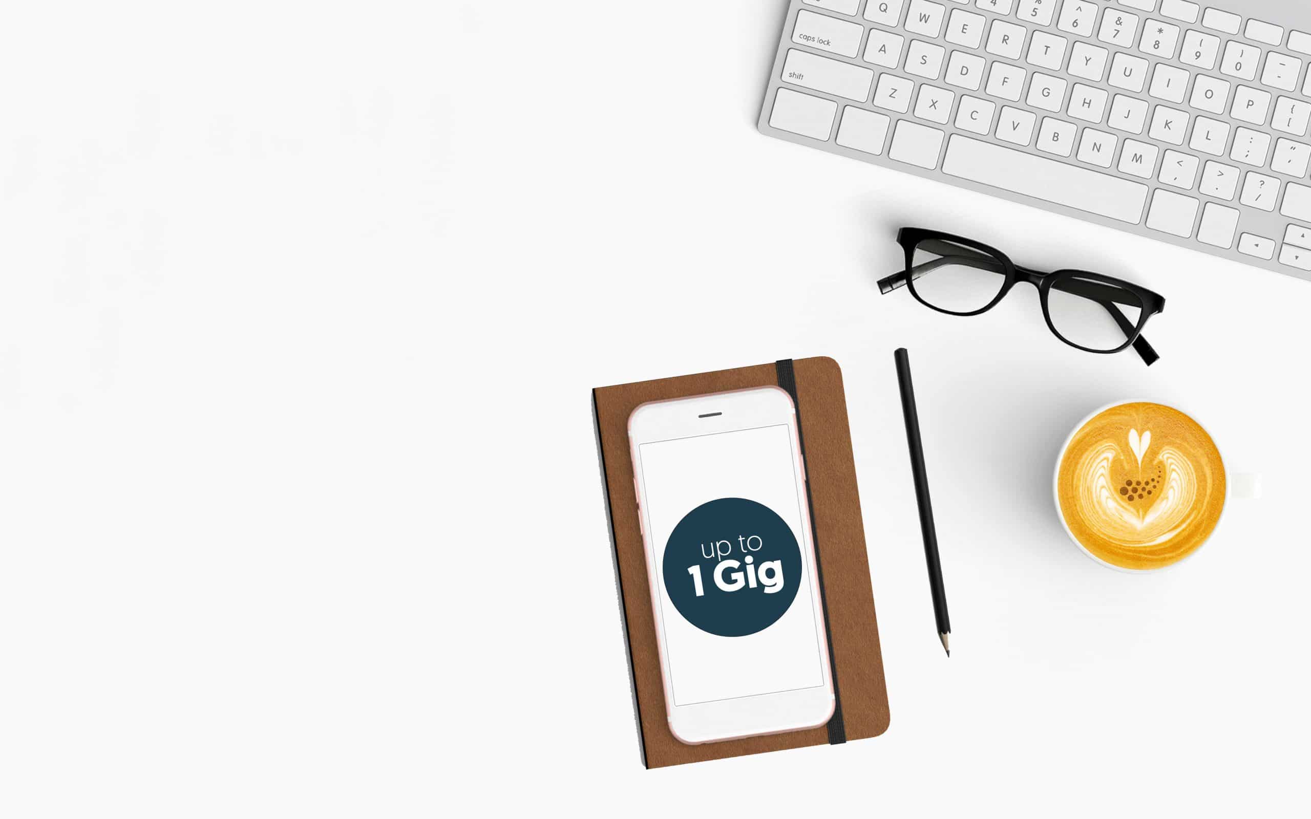 Image of keyboard, smart phone, and desk items beside a latte